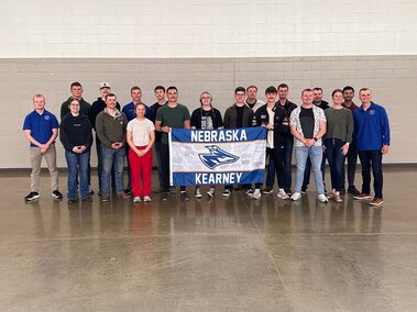 Group of people standing indoors holding a Nebraska Kearney flag.